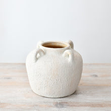 Textured white ceramic vase with small decorative handles and a rounded shape, featuring a rustic stone-effect finish on a wooden surface.