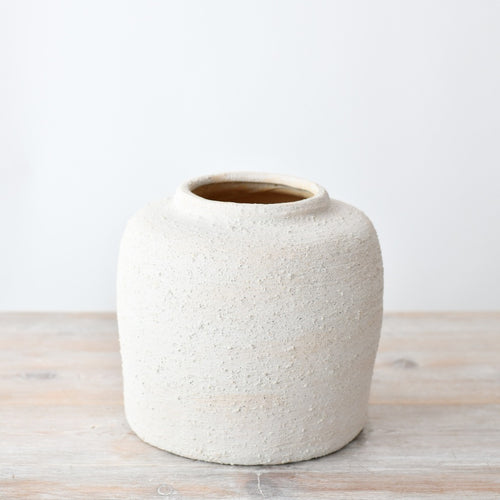 Textured white ceramic vase with a rounded minimalist shape, featuring a natural stone-effect finish, styled on a wooden surface.