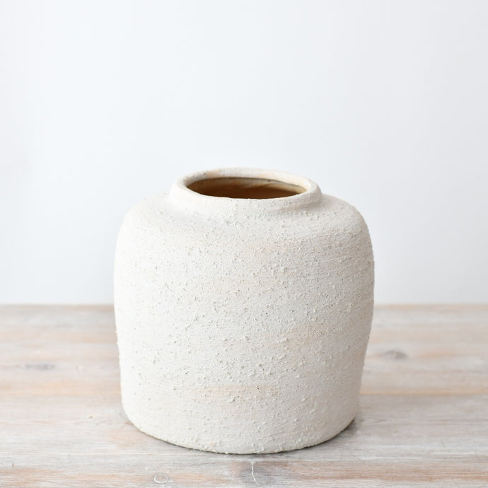 Textured white ceramic vase with a rounded minimalist shape, featuring a natural stone-effect finish, styled on a wooden surface.