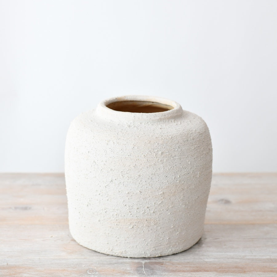 Textured white ceramic vase with a rounded minimalist shape, featuring a natural stone-effect finish, styled on a wooden surface.